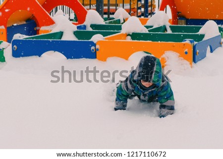 Boy crawling through the snowdrifts on the playground.