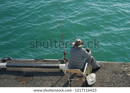 fisherman sitting on the pier at the blue calm sea and catching fish