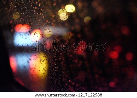 Rain drops on the window and bokeh of night lights in the background with film grained effect.