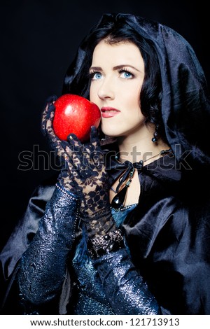 Woman in black cloak with hood holding red apple