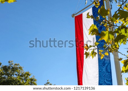 The Netherlands flag against a clear blue sky in autumn