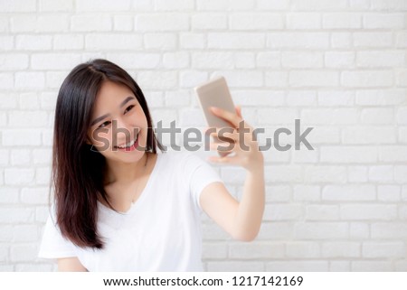 Beautiful portrait young asian woman taking a selfie with smart mobile phone on concrete cement white background, girl is photographing with happy and smile with fun, lifestyle concept.