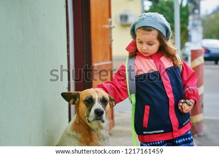 A girl and a stray dog . A small child is petting a stray dog