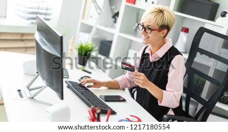A young girl sitting at a computer table and holding a Bank card.