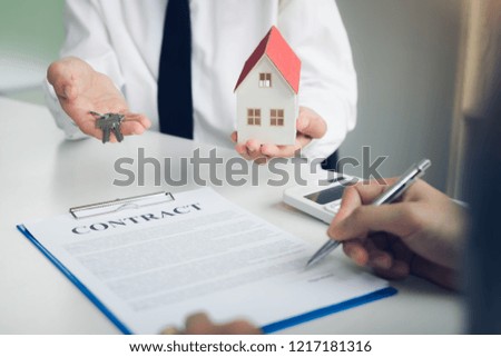 Customer writing signing signature on paper contract with real estate agent and giving key to client.