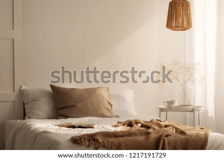 Closeup of bed with beige blanket and linen pillow in minimal bedroom interior, real photo with copy space on the empty wall
