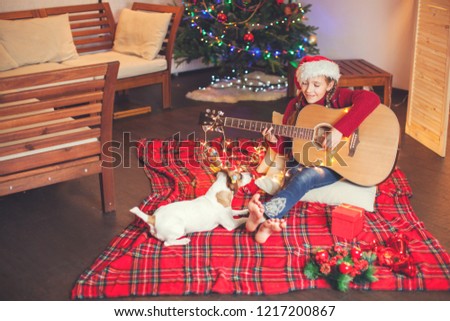Girl with a dog playing the guitar and singing near christmas tree. Happy New Year