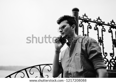 Indian man at red shirt and sunglasses posed outdoor and speaking on phone. Black and white photo.