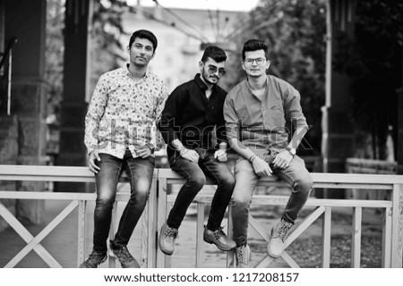 Three indian guys students friends sitting on street. Black and white photo.