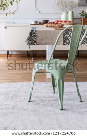 Mint green chair on grey carpet at table in rustic dining room interior with lamp and wall with molding. Real photo