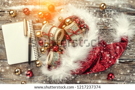 Old wooden Christmas background, Santa Claus hat full of baubles and money. Top view. Space for text. Effect of light and snowflakes.