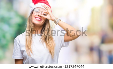 Young beautiful woman wearing christmas hat over isolated background doing ok gesture with hand smiling, eye looking through fingers with happy face.