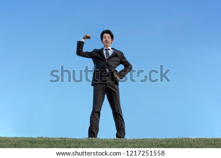 A young businessman wearing a suit that making guts pose with the blue sky background. Energy, success, fighting spirit, challenging image