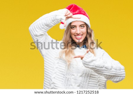 Beautiful young blonde woman wearing christmas hat over isolated background smiling making frame with hands and fingers with happy face. Creativity and photography concept.