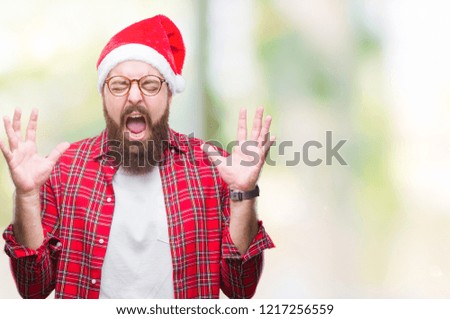Young caucasian man wearing christmas hat over isolated background celebrating mad and crazy for success with arms raised and closed eyes screaming excited. Winner concept