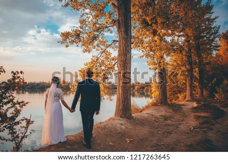 Bride and groom under orange autumn trees, lake and sunset in background