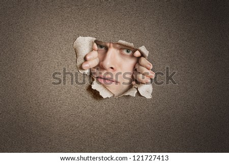 Portrait of a young Caucasian man peeking from ripped white paper hole
