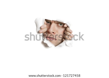 Portrait of a young Caucasian man peeking from ripped white paper hole