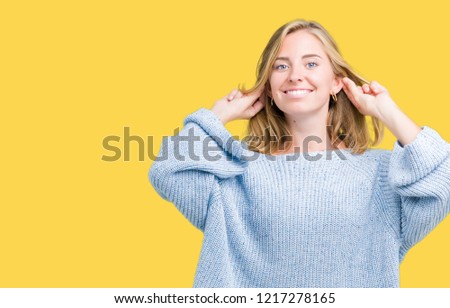Beautiful young woman wearing blue sweater over isolated background Smiling pulling ears with fingers, funny gesture. Audition problem
