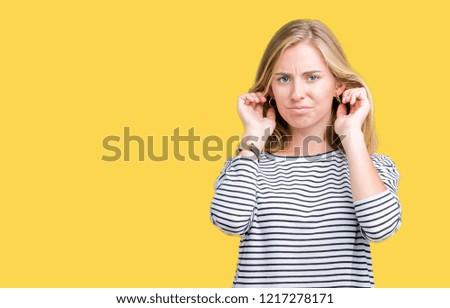 Beautiful young woman wearing stripes sweater over isolated background covering ears with fingers with annoyed expression for the noise of loud music. Deaf concept.
