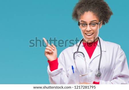 Young afro american doctor woman over isolated background with a big smile on face, pointing with hand and finger to the side looking at the camera.