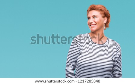 Atrractive senior caucasian redhead woman over isolated background looking away to side with smile on face, natural expression. Laughing confident.