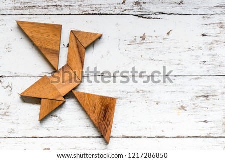 Tangram puzzle in flying bird shape on old white wood background
