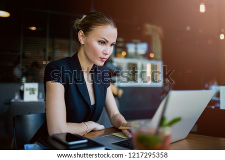 Woman professional economist checking e-mail on laptop computer while sitting in restaurant during work break in company. Female experienced business writer for executive summary using netbook 