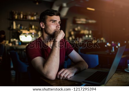 Young man skilled content writer thinking about new ideas while sitting with portable laptop computer in restaurant. Thoughtful men publication specialist dreaming during work on modern notebook 