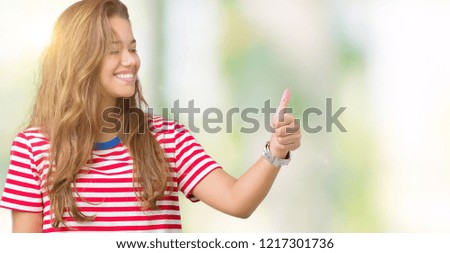 Young beautiful brunette woman wearing stripes t-shirt over isolated background Looking proud, smiling doing thumbs up gesture to the side