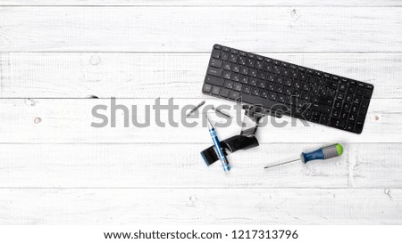 Old broken black laptop keyboard, an electronic printed circuit board, screwdrivers on a wooden white table. Copy space for your text