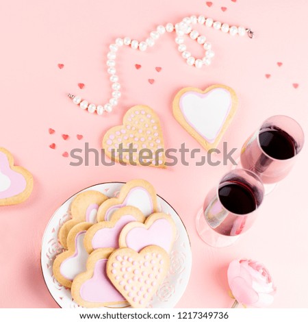 Valentine's day cookies, wine glasses and wine on pink background.