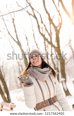 Attractive young woman leaning against a wooden fence in a park, enjoying a snowy winter day in nature