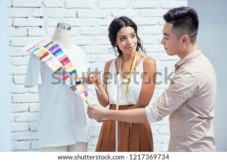 Young female designer suggesting to choose a color for the shirt to her client in studio