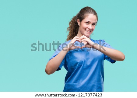 Young brunette doctor girl wearing nurse or surgeon uniform over isolated background smiling in love showing heart symbol and shape with hands. Romantic concept.