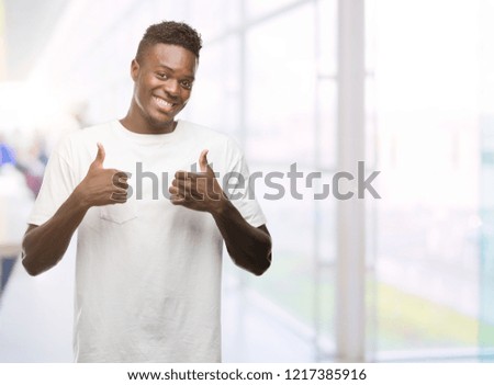 Young african american man wearing white t-shirt success sign doing positive gesture with hand, thumbs up smiling and happy. Looking at the camera with cheerful expression, winner gesture.