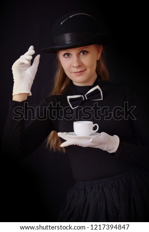 Actress in black hat and black suit holding a tea pair