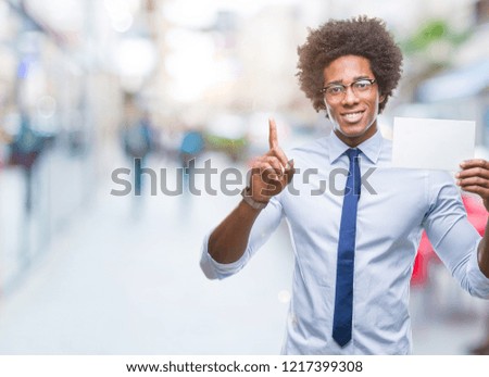 Afro american man holding blank card over isolated background surprised with an idea or question pointing finger with happy face, number one
