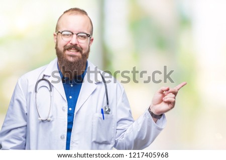 Young caucasian doctor man wearing medical white coat over isolated background with a big smile on face, pointing with hand and finger to the side looking at the camera.