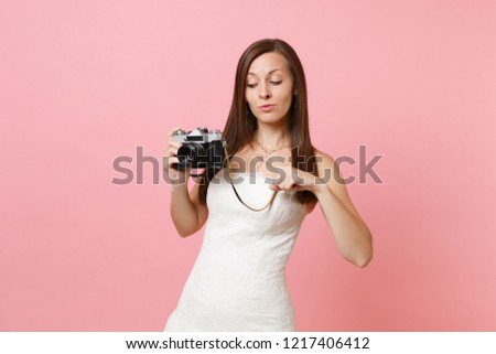 Pretty bride woman in white wedding dress pointing index finger on retro vintage photo camera choosing staff, photographer isolated on pink background. Wedding to do list. Organization of celebration