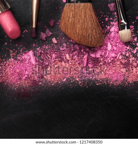 A closeup photo of makeup brushes and lipstick, with vibrant pink and purple eye shadow shot from the top on a black background with copy space