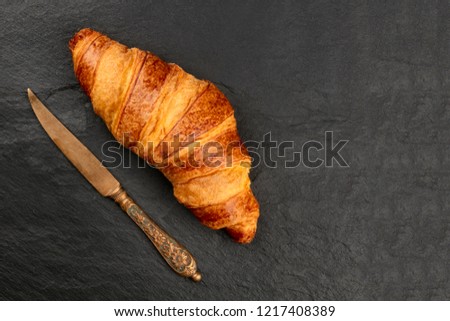A photo of a croissant with a vintage table knife, shot from above on a black background with a place for text
