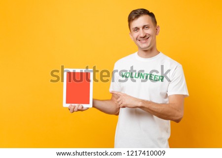 Man in white t-shirt written inscription green title volunteer hold tablet pc computer with blank empty screen isolated on yellow background. Voluntary free assistance help charity grace work concept