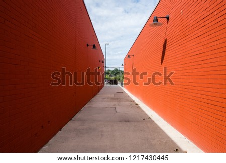 Street photography of abstract long alleyway. Pathway between two buildings with red brick wall facade. Minimal street photography. Light and shadow on brick wall exteriors.  