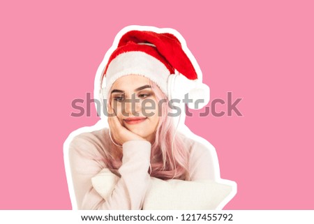 Attractive smiling young girl dressed in Santa's hat listening the music by headphones and dreams about gifts. Christmas and New Year advertising concept isolated on abstract blurred white background