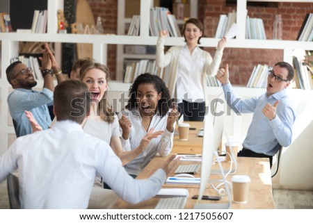 Male worker share good news with multiracial colleagues in shared workplace, diverse employees scream with happiness excited with corporate success or goal achievement, team celebrating win Royalty-Free Stock Photo #1217505607
