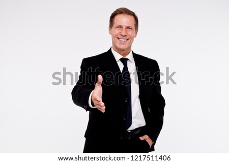 Nice to meet you! Handsome man in suit greeting you with hand and looking at camera with smile while standing against white background
