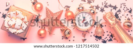Christmas or New Year composition, frame, pink background with gold Christmas decorations, stars, snowflakes, balls, alarm clock, gift box and bottle of champagne, banner, top view