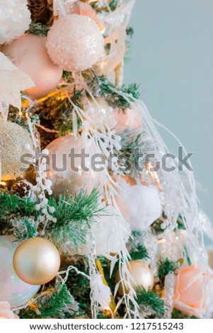 Christmas tree with toys and Christmas balls of soft pink and golden colors with illuminated  shimmering garlands against a blue wall picture with grain close-up