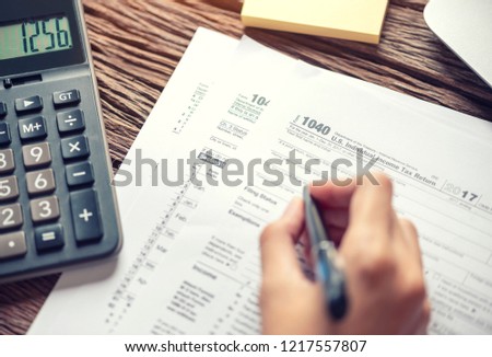 Woman hand writing U.S. tax form 1040, using calculator Individual income tax return, taxation without representation, time to payment concept. Royalty-Free Stock Photo #1217557807